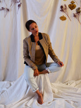 Load image into Gallery viewer, Lady sat down wears Sunset jacket made of plaid fabric with contrasting black collar, and black button stand. Details cuff belts like a trench coat.