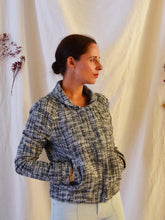 Load image into Gallery viewer, Lady stands wears Sunset jacket made from a black, white, grey wooden fabric, with hands in pockets.