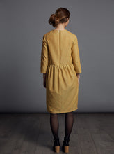 Load image into Gallery viewer, Back view shows drop shoulders at back, with gathered waistline and invisible zip at centre back seam of the knee-length dress.