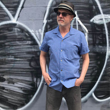 Load image into Gallery viewer, Man stands in front of graffiti wall wearing Tropical short-sleeve shirt with one chest pocket in a blue check fabric.