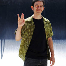 Load image into Gallery viewer, Man stands wearing Tropical short-sleeve shirt with one chest pocket in a yellow green spot pattern fabric. Shirt worn open revealing a plain black t-shirt underneath.