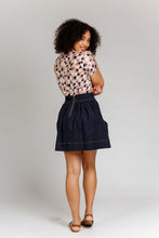 Load image into Gallery viewer, Back view of lady wearing a denim, short Brumby Skirt with contrasting topstitching detail. Exposed metallic zip at waistband.
