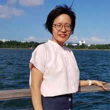 Load image into Gallery viewer, Lady stands by rail, wearing a Sille Shirt in a solid colour fabric, tucked into trousers.