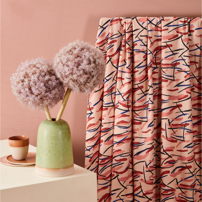 Viscose Twill fabric with a marker/brushstroke chaotic print hangs by a table with a vase