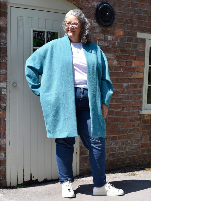 Lady stands in front of a wooden door wearing a cocoon shaped Wimborne coat open.