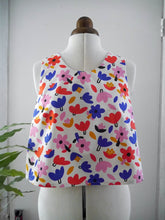 Load image into Gallery viewer, A sleeveless white top with a colourful abstract floral and leaf print, displayed on a mannequin.
