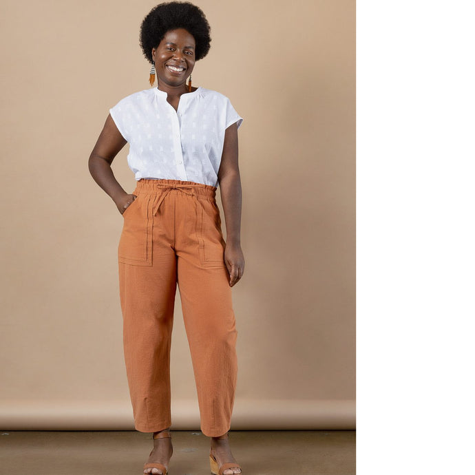 Model wears barrel leg trousers with large patch pockets and drawstring paperbag waist