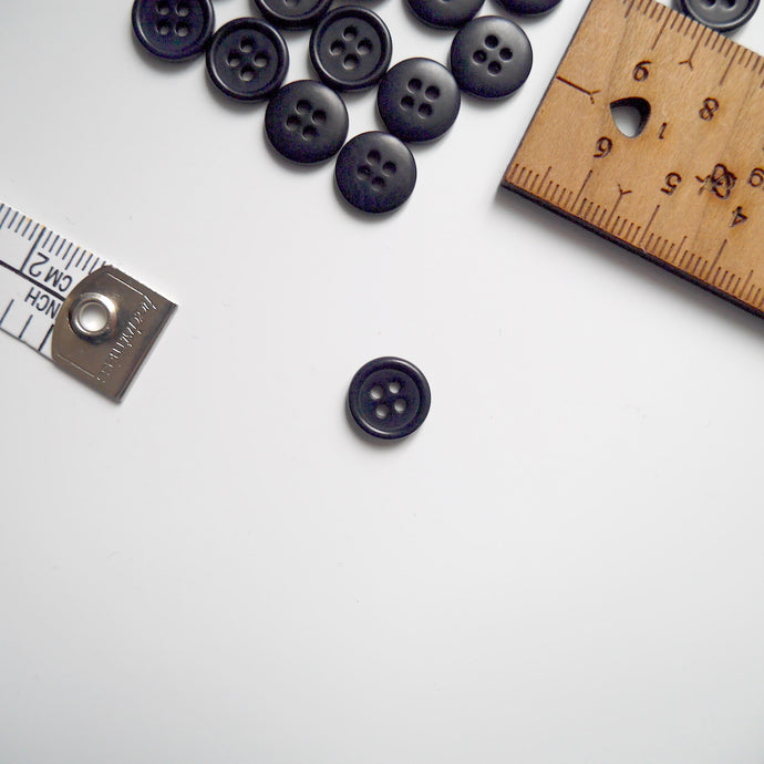 Corozo button with 4 holes, displayed amongst tape measure and ruler