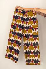 Load image into Gallery viewer, Hands holding up a pair of Flâneur trousers, front view, in busy print fabric, with patch pockets at sides
