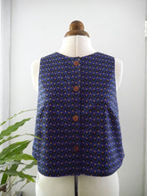 Load image into Gallery viewer, A sleeveless vest with a small repeating geometric pattern displayed on a mannequin. The vest features three buttons down the centre front.
