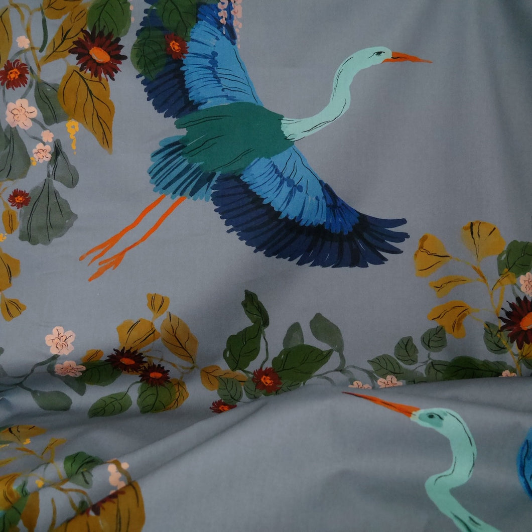 Cotton fabric with pattern print of large heron in flight amongst leaves, displayed in drape