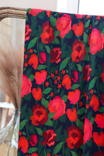 Load image into Gallery viewer, Floral viscose fabric with red flowers on a dark background draped over a chair.
