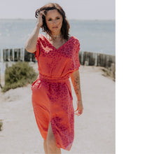 Load image into Gallery viewer, Lady at the beach walks, wearing a V-neck, short sleeved, knee length dress with waist tie
