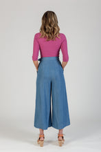 Load image into Gallery viewer, Back view of lady wearing cropped wide-leg trousers with hands in side pockets
