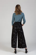 Load image into Gallery viewer, Back view of lady wearing a pair of wide-leg trousers, with hands in side pockets
