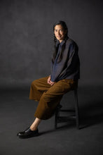 Load image into Gallery viewer, Model sits in stool wearing wide-leg culotte trousers in a cord fabric
