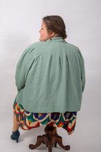 Load image into Gallery viewer, Back view of model sitting, wearing a loose-fitting jacket with sunburst tucks around the neckline
