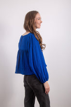 Load image into Gallery viewer, Model is wearing a long-sleeved blouse that has a gathered detail at the yoke, creating a slightly voluminous shape. The sleeves are full and gathered at the wrists. 
