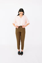 Load image into Gallery viewer, Lady stands in front profile wearing Palisade Pants, a tapered trouser with cross over panel detail pockets at hip level
