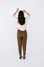 Load image into Gallery viewer, Lady stands with back profile wearing Palisade Pants, a tapered trouser with cross over panel detail pockets at hip level
