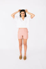 Load image into Gallery viewer, Lady stands in front profile wearing Palisade Shorts, mid-thigh shorts with cross over panel detail pockets at hip level
