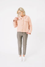 Load image into Gallery viewer, Lady wears Papercut Stacker Jacket pattern, a utility jacket with flapped in-seam pockets on front, worn fastened, lifts pocket flap to reveal contrasting lining fabric
