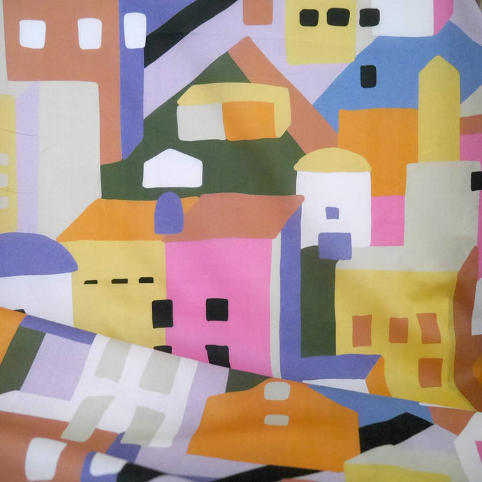 Cotton Lawn fabric with a colourful abstract pattern of geometric shapes resembling buildings, displayed with drape