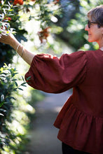 Load image into Gallery viewer, Image of lady picking a leaf on a hedge, shows off puffy sleeve, and gathered peplum detail
