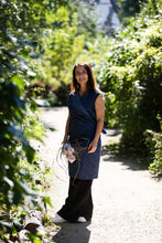 Load image into Gallery viewer, Lady wears a wrap dress over a pair of trousers, stands amongst green hedges
