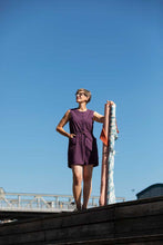 Load image into Gallery viewer, Lady stands on wooden platform wearing a sleeveless button up bodice jumpsuit with thigh length shorts
