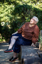 Load image into Gallery viewer, Lady sits on wooden bench laughing, wearing a scoop neck top, with a midi denim skirt with centre front split seam
