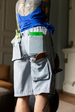 Load image into Gallery viewer, Lower view photo of model wearing elasticated knee-length shorts with multiple pockets, filled with household items
