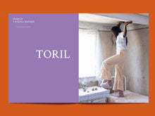 Load image into Gallery viewer, Magazine spread features a bold title: &quot;Toril&quot; alongside photo of lady standing on bed showing off wide legged trousers with ruffle hem
