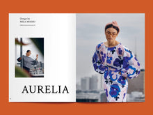 Load image into Gallery viewer, Magazine spread features title: &quot;Aurelia&quot; alongside photo of lady wearing a puffy sleeve dress in large abstract print
