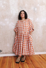 Load image into Gallery viewer, Lady wears loose short sleeved gingham dress, gathered skirt at waist, hands in side pockets of skirt
