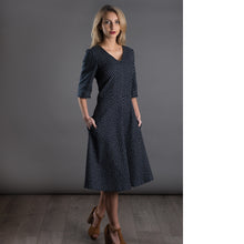 Load image into Gallery viewer, Lady wears V-neck dress with A-line skirt, hands in pockets of skirt
