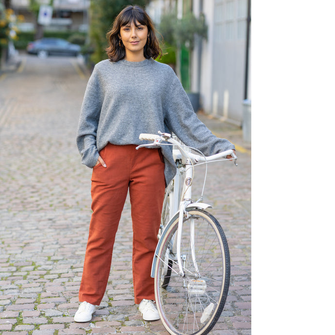 Lady stands next to bike wearing The City Trousers, a slim leg with hand in pocket