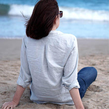 Load image into Gallery viewer, Lady sits on beach wearing Anna shirt, back view shows inverted pleat at yoke.
