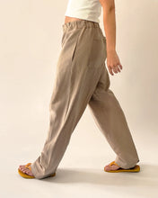 Load image into Gallery viewer, View of model mid stride, wearing elasticated waist trousers with curved legs, inseam side pocket, and back patch pocket
