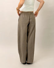 Load image into Gallery viewer, Back view of model wearing elasticated waist trousers with curved legs, and back patch pockets
