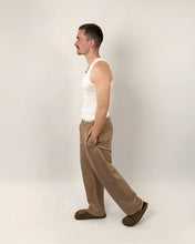 Load image into Gallery viewer, View of model mid-stride wearing elasticated waist trousers with curved legs, with hands in inseam side pockets
