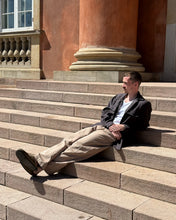 Load image into Gallery viewer, Model leans on stairs, wearing trousers with curved legs
