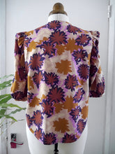 Load image into Gallery viewer, Back view of a short-sleeve blouse with puff sleeves and a retro floral pattern, displayed on a mannequin. The pattern features starburst flowers.
