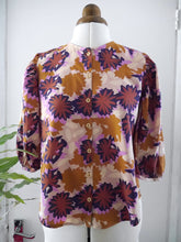 Load image into Gallery viewer, A vintage-style floral blouse with three-quarter puff sleeves, displayed on a mannequin. The blouse features a retro pattern of starburst flowers, with a button-up front.
