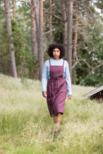 Load image into Gallery viewer, Lady walks through field wearing an apron dress over a long sleeved top.
