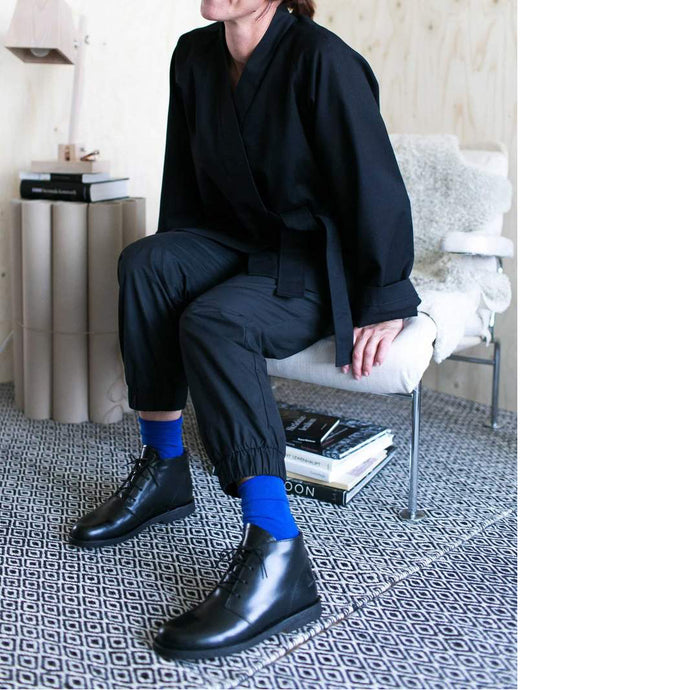 Lady sat on chair showing off her elastic cuff trousers and wrap jacket with royal blue socks and black shoes