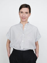 Load image into Gallery viewer, Lady smiles wearing the Cap Sleeve Shirt in a fine stripe pattern tucked into trousers
