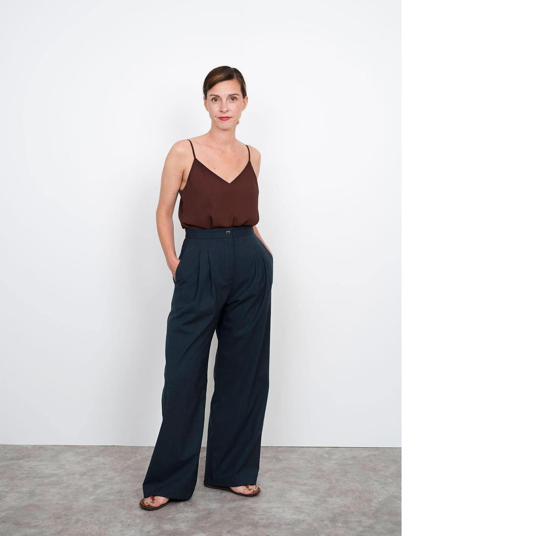 Lady stands wearing high waisted trousers, wide leg with pleats at waistline