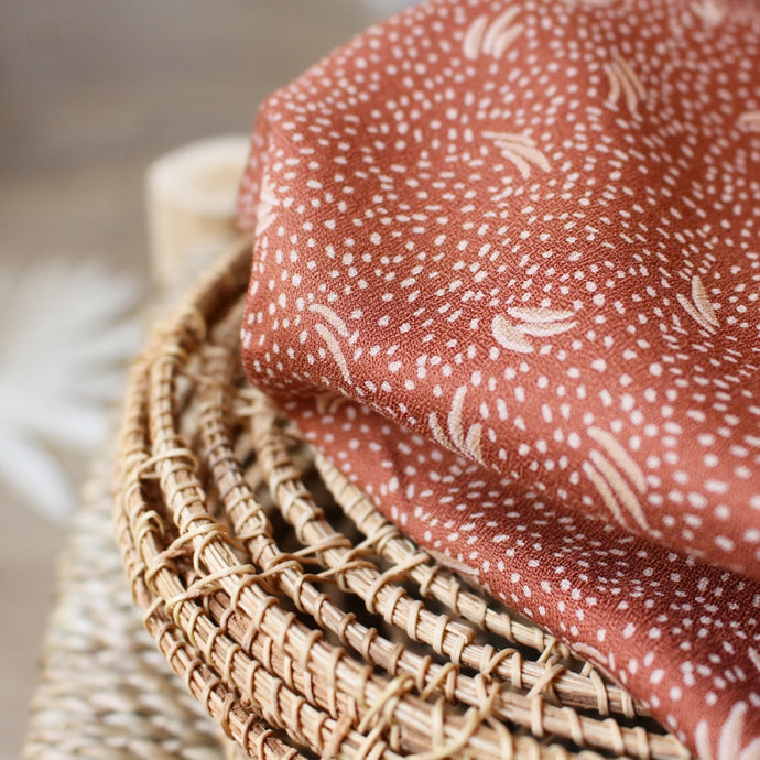 Viscose Crepe Fabric with dots and leaf motifs sits on top of a wicker piece
