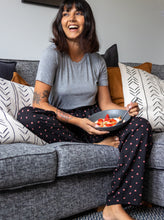Load image into Gallery viewer, Lady sat on couch with bowl of cereal laughing, wearing The Pyjama Bottoms in spotty fabric.
